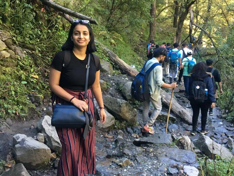 Female trekker smiling along a forested trail by a small stream on Kheerganga trek
