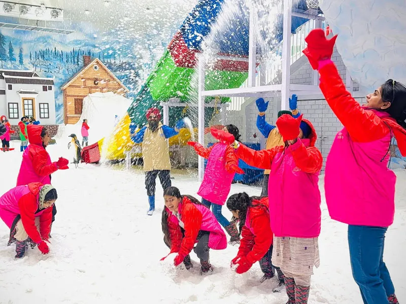 Tourists in bright pink winter jackets enjoying artificial snowfall inside an adventure snow amusement park