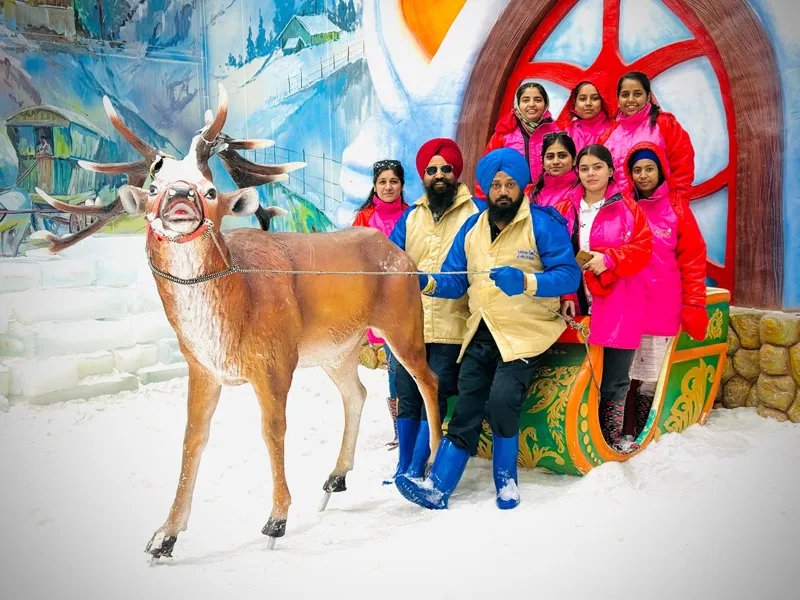 Family posing in colorful winter parkas with a life-sized reindeer statue at an indoor snow park