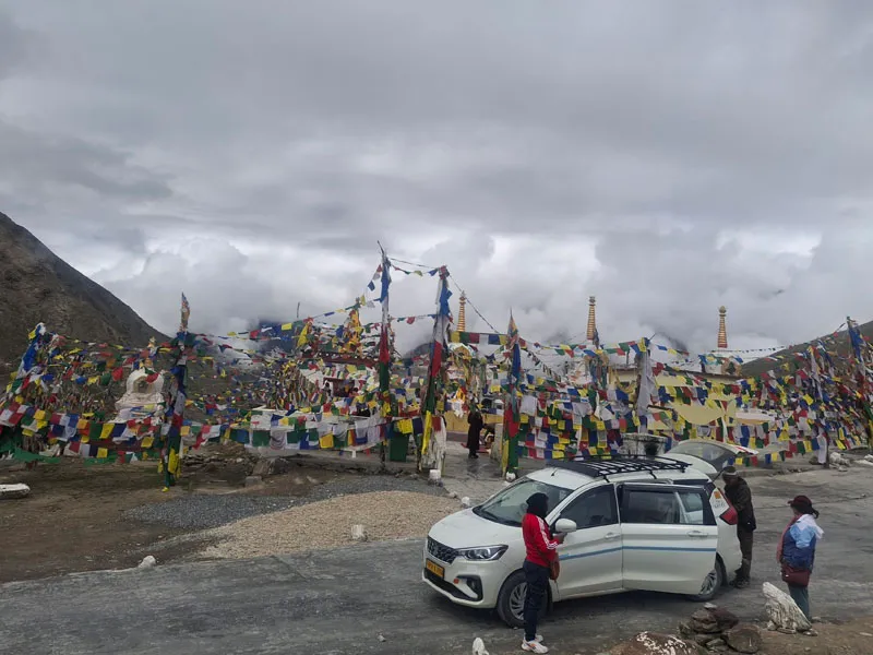 White car parked at Kunzum Pass surrounded by hundreds of vibrant Tibetan prayer flags