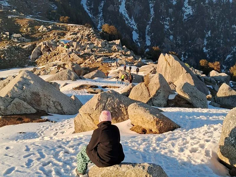Trekker sitting on a boulder facing snow-covered slopes and rocky moraines near Laqa Glacier