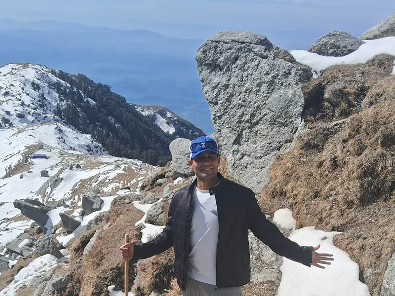 Hiker posing beside a massive rock monolith along the snow-covered mountain pass trail