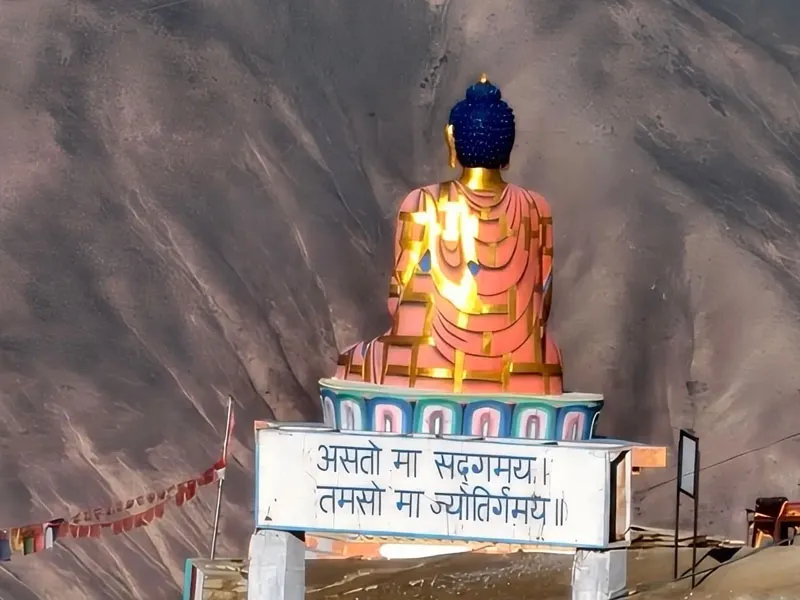 Colossal colorful Buddha statue overlooking rugged barren canyon cliffs at Langza village Spiti