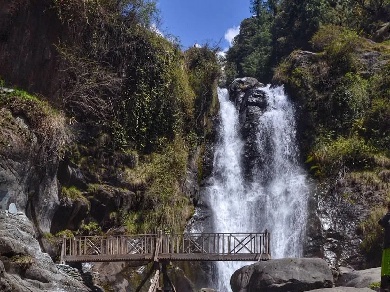 Lapas Waterfall cascading into a mountain pool with a wooden pedestrian bridge in front