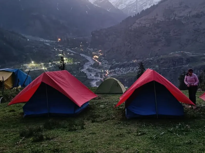 Red and blue alpine dome tents pitched at high-altitude campsite overlooking Kullu valley