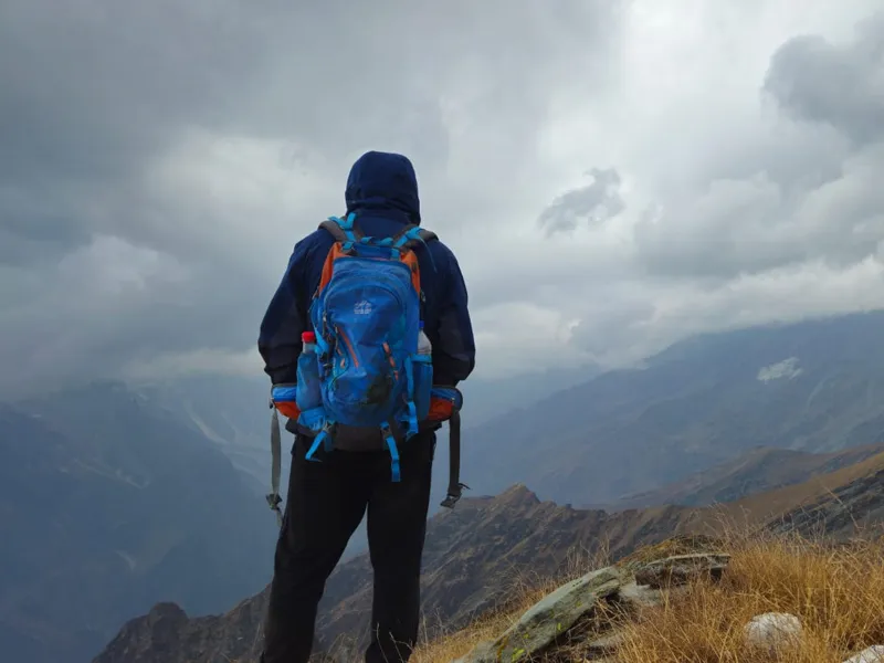Hiker with blue backpack standing on mountain edge looking out over vast misty valleys