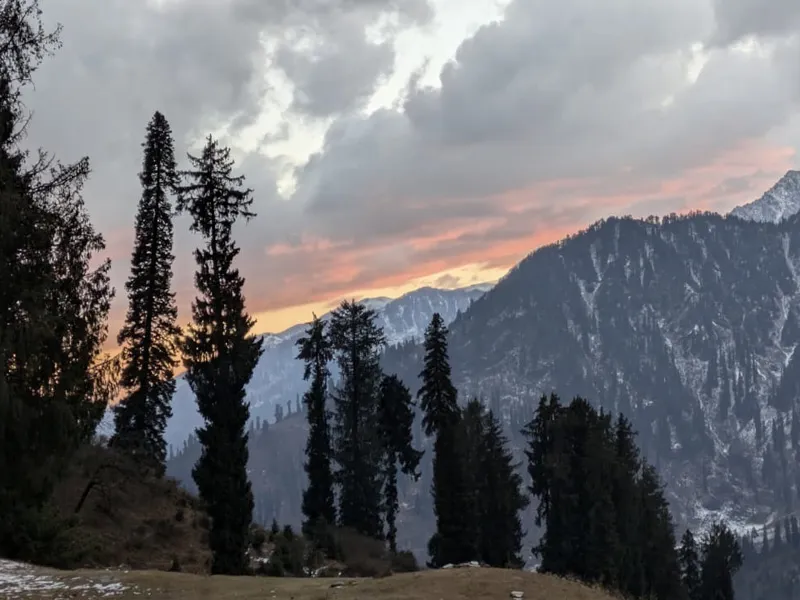Dramatic golden sunset and dark storm clouds over pine-covered mountain ridges near Patalsu Peak