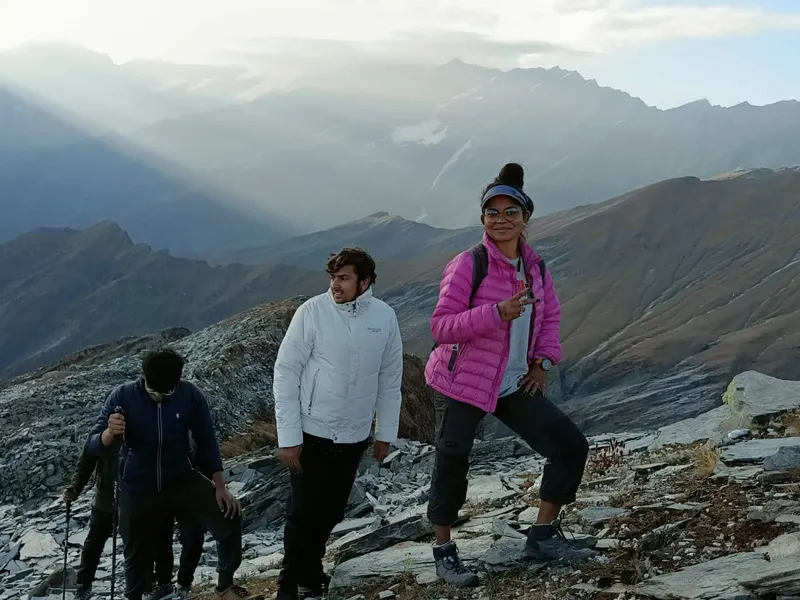 Trekkers pausing on a high rocky ridge with sunbeams breaking over layered mountain peaks