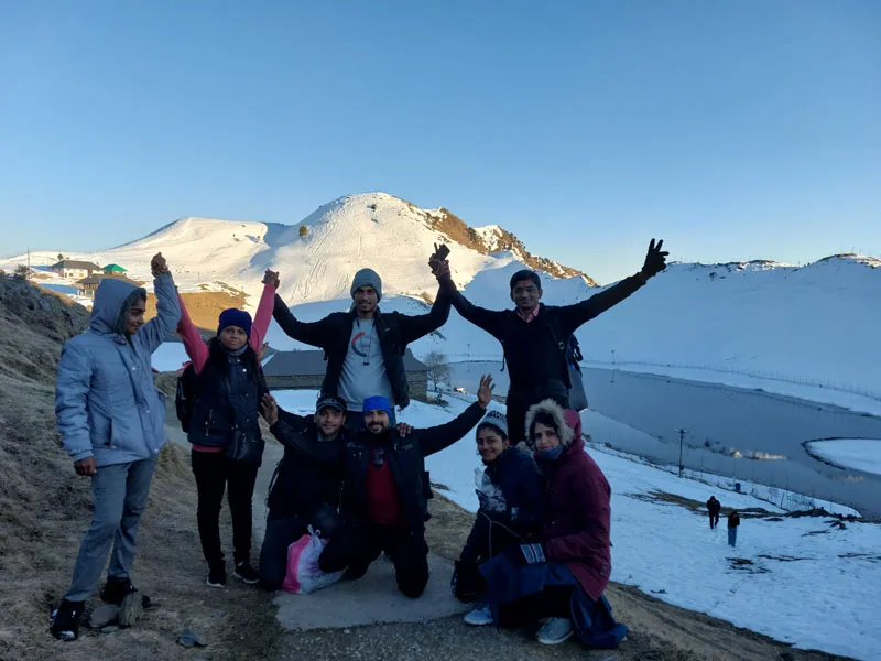 Group of trekkers cheering on snow-covered slopes overlooking Prashar Lake basin
