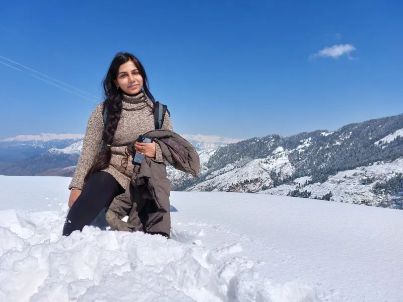 Woman sitting in deep winter snow against clear blue sky on Prashar Lake trek
