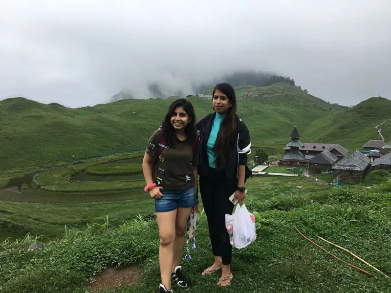 Two female hikers smiling together on vibrant green hillside pastures near Prashar Lake