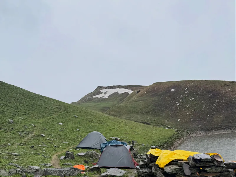 Alpine campsite with tents pitched on a green meadow near a mountain pond along Ranisui Lake trail