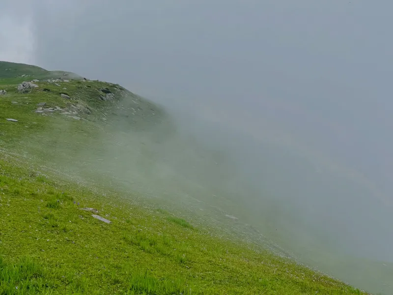 Dense fog and mist rolling over green mountain slopes and ridge near Ranisui Lake