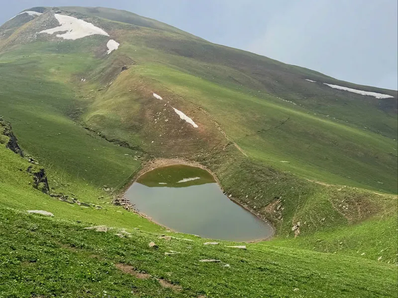 Top-down scenic view of tranquil Ranisui Lake nestled between rolling green hills with snow patches