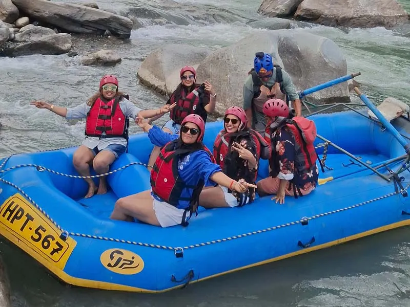 Tourists in life jackets and helmets enjoying white water river rafting in a blue raft on Beas River