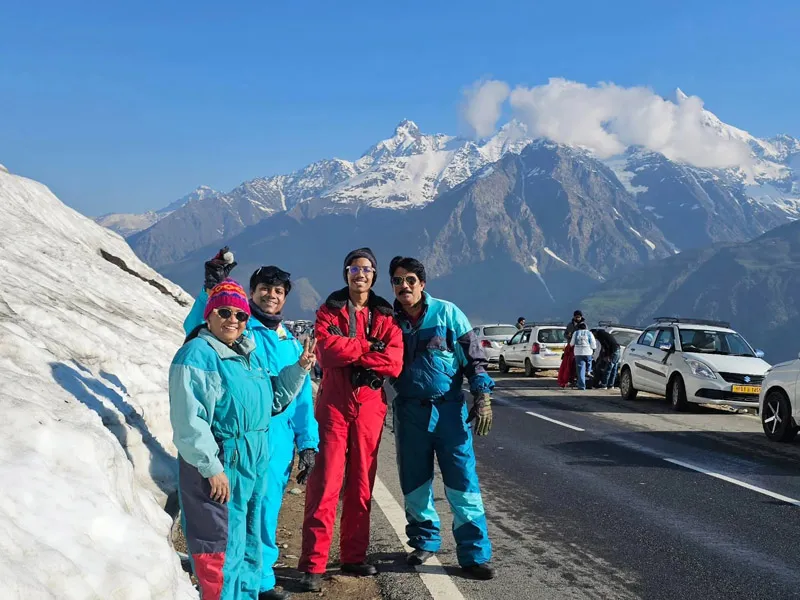Tourists in colorful snowsuits posing along a high mountain road against snow-capped Himalayan peaks