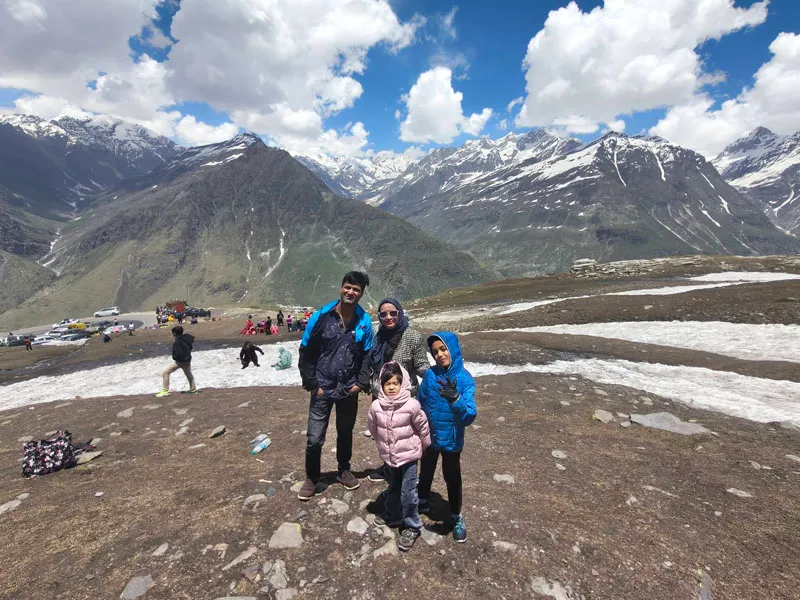 Family posing on snow-covered slopes with majestic Himalayan mountain peaks at Rohtang Pass