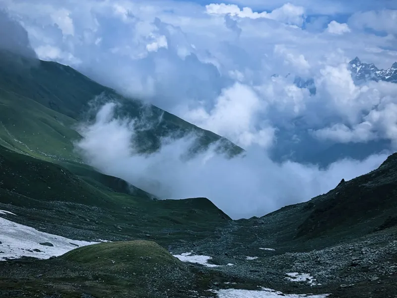 Dramatic view of white clouds floating through lush green mountain valley along Sar Pass trail