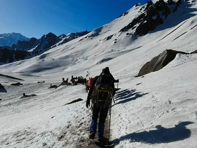 Trekker with backpack walking across steep snow slopes leading towards Sar Pass