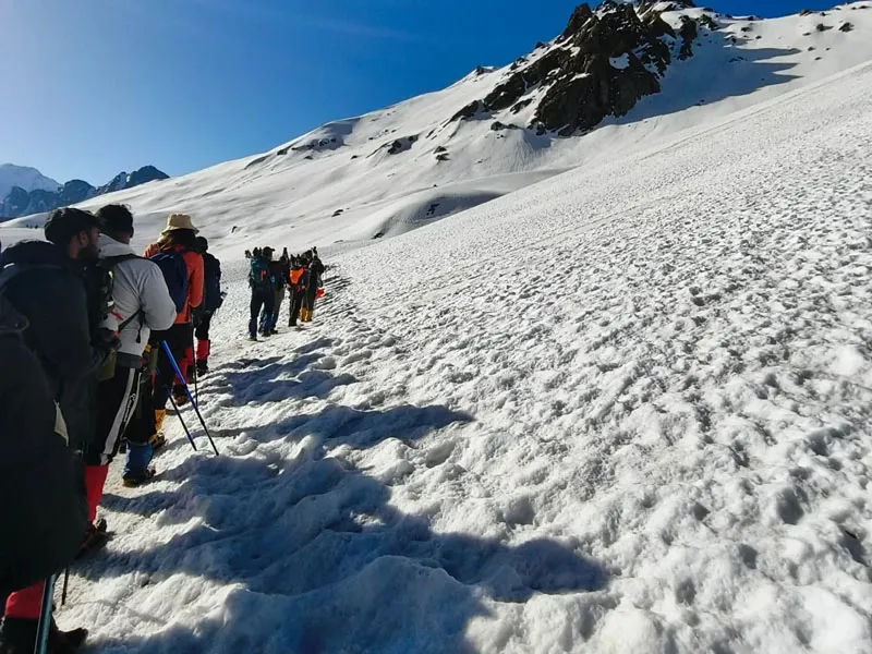 Group of trekkers walking single file along a deep snowy mountain track on Sar Pass trek