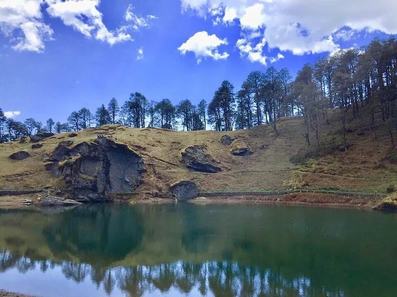 Calm reflective emerald waters of Serolsar Lake bordered by dense oak and pine forest
