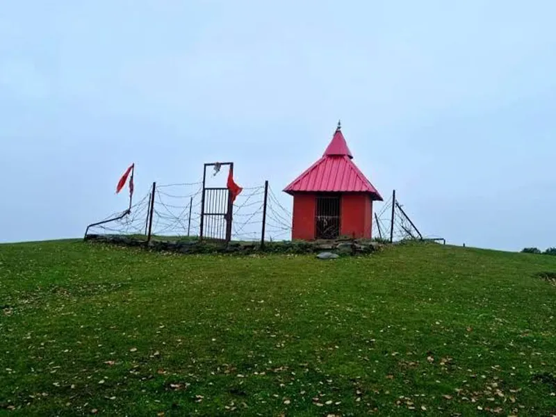 Small red-roofed mountain shrine perched atop a lush green alpine meadow clearing