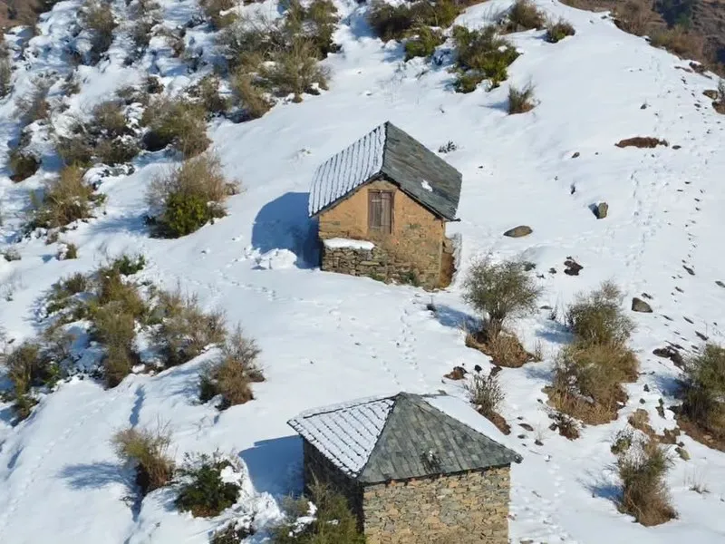Traditional stone shepherd huts nestled on hillside blanketed in deep winter snow