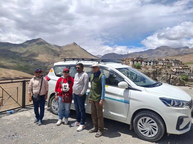 Travelers posing with an SUV tour vehicle at a scenic mountain viewpoint in Spiti Valley