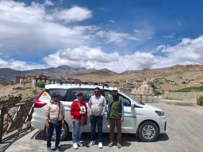 Travelers posing next to a white SUV on a scenic mountain road in Spiti Valley