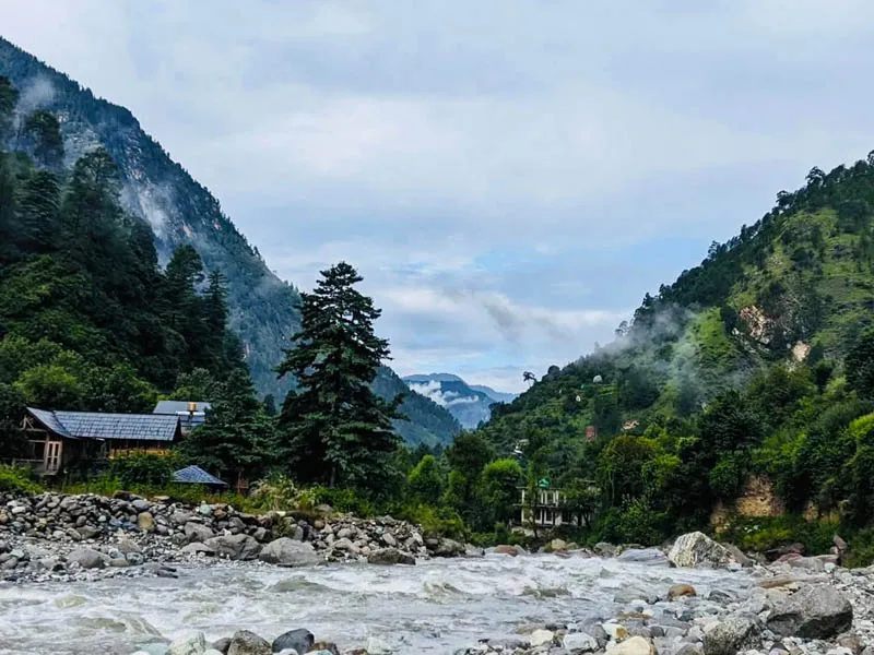 Pristine Tirthan River flowing over riverbed stones between steep forested Himalayan hillsides