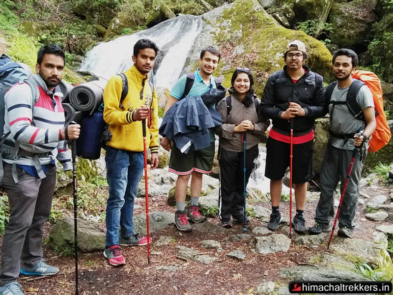 Trekking group with backpacks and trekking poles posing near a river in Tirthan Valley