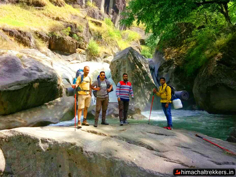 Hikers crossing giant boulders near a cascading mountain stream in Great Himalayan National Park
