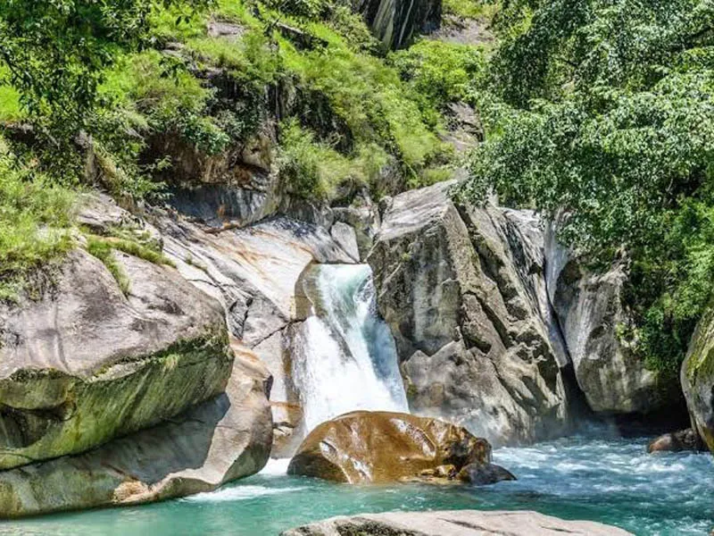 Crystal-clear waterfall cascading over smooth rocky gorge into a natural pool in Tirthan Valley