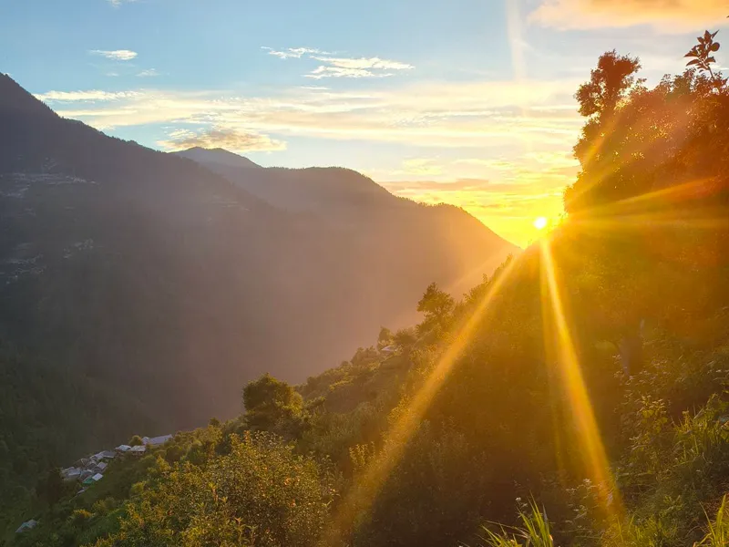 Golden sunrise rays illuminating the misty mountain valley and ridges in Tirthan