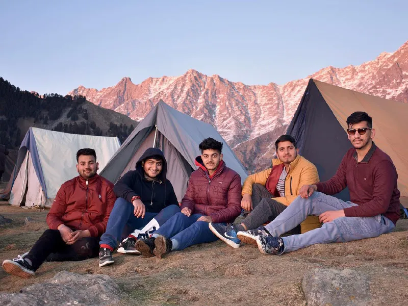 Group of friends relaxing outside camping tents on the Triund ridge during sunset