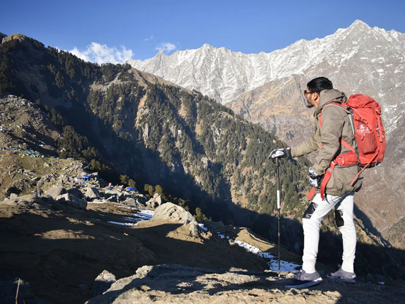 Trekker with backpack standing on high mountain ridge looking towards rugged snow-dusted slopes