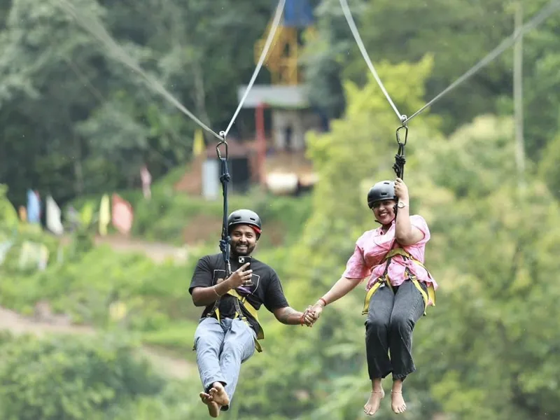 Two adventure enthusiasts gliding on a tandem zipline wire over lush green valley in Manali