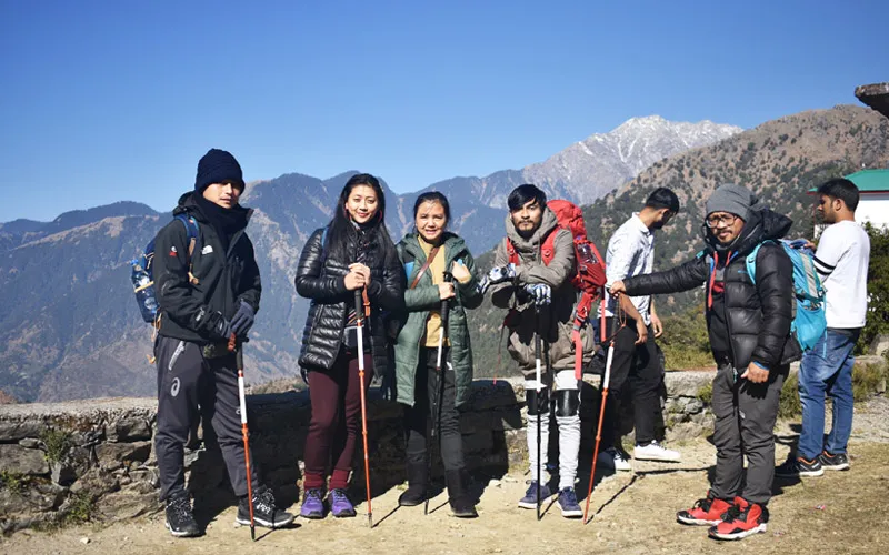 Group of trekkers with walking poles posing on a scenic mountain ridge on Triund trek