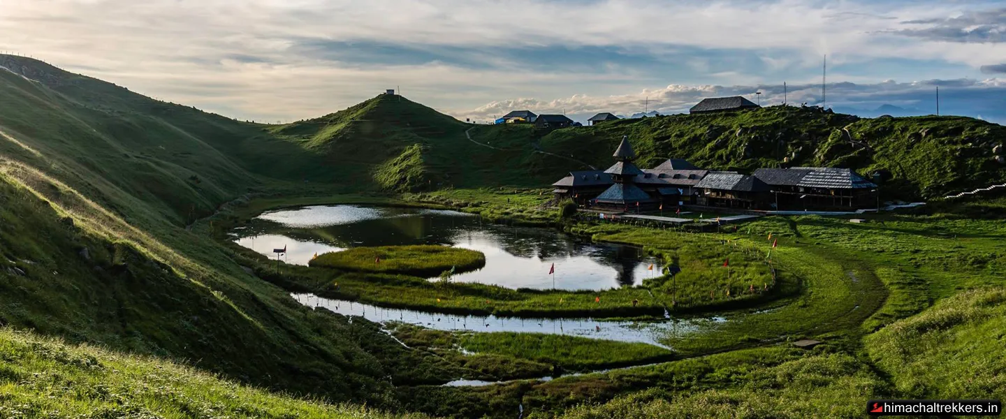 Pristine Prashar Lake basin surrounded by green rolling hills and traditional wooden temple
