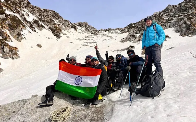 Trekking team holding the Indian national flag at snow-clad Indrahar Pass summit