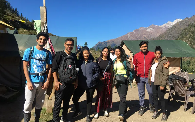 Group of trekkers standing together at Kheerganga base campsite with mountains in the background