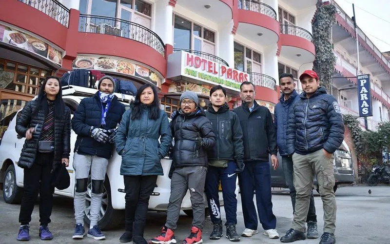 Group of travelers posing together on a hill station street outside hotel buildings