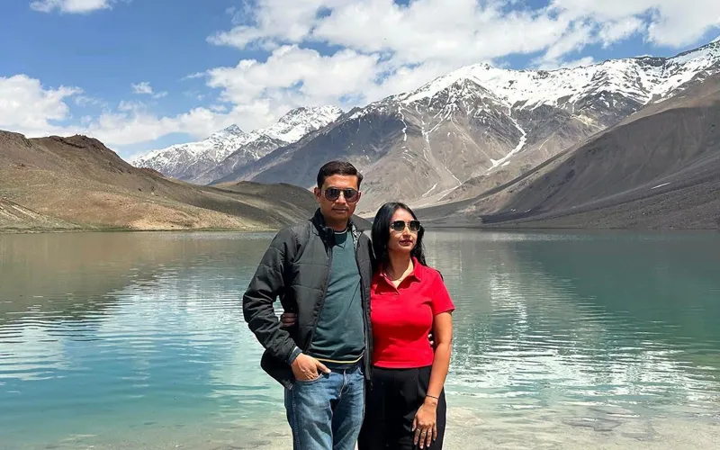 Honeymoon couple standing by scenic high-altitude Himalayan lake with snow-covered mountains in Manali