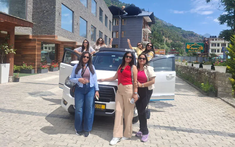 Travelers posing beside an open convertible car on a scenic mountain road in Manali