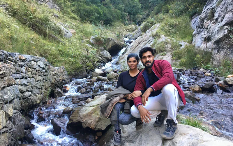 Hikers sitting and resting beside a rocky mountain stream along the Kheerganga trek