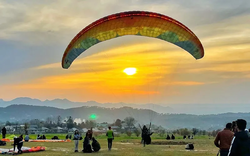 Paraglider soaring under a yellow and red canopy above the landing site in Bir Billing
