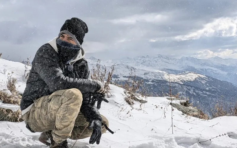 Trekker bundled up in warm winter gear crouching on snow-covered slopes on Patalsu Peak trek