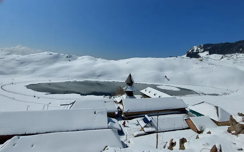 Frozen, snow-covered landscape surrounding Prashar Lake and nearby mountain huts in winter