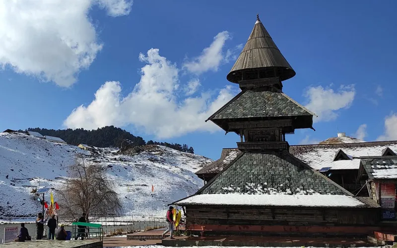 Three-tiered wooden pagoda roof of Prashar Rishi Temple against snow-dusted slopes and blue sky
