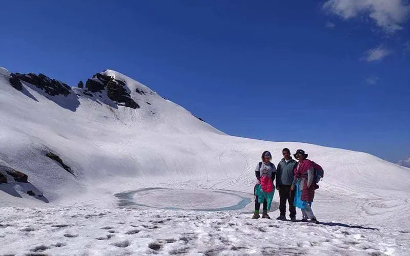 Trekkers standing together on an expansive snow slope beneath a clear blue sky on Ranisui Lake trek